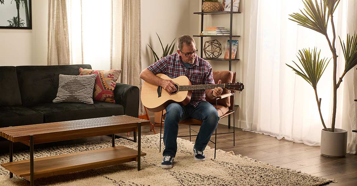 Man on stool playing Taylor A12E in Living Room